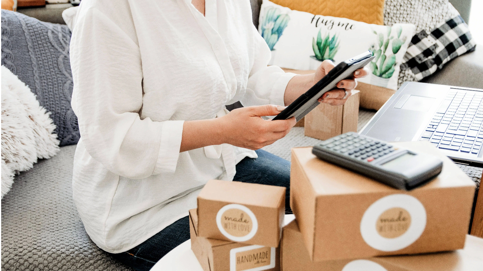 Woman in white blouse handling online business orders with tablet boxes and calculator